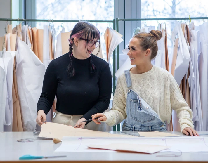 Two fashion students laughing while working on design patterns in a classroom. Two fashion students laughing while working on design patterns in a classroom.